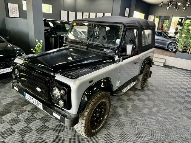 A silver and black Land Rover Defender 90 with a soft top in the showroom